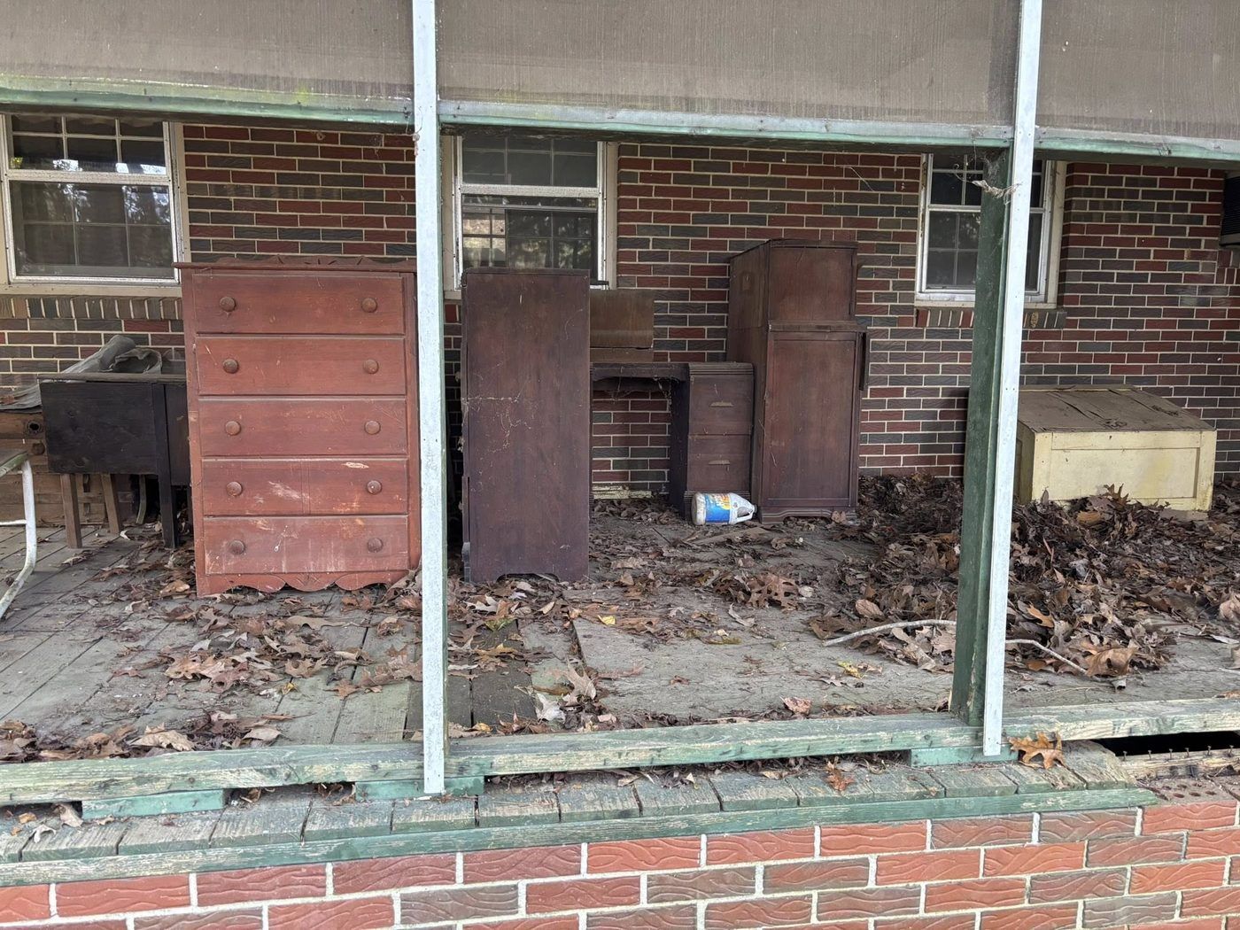 A covered porch stacked with old dressers, cabinets and leaf debris before a Dutch Dumpsters cleanout.