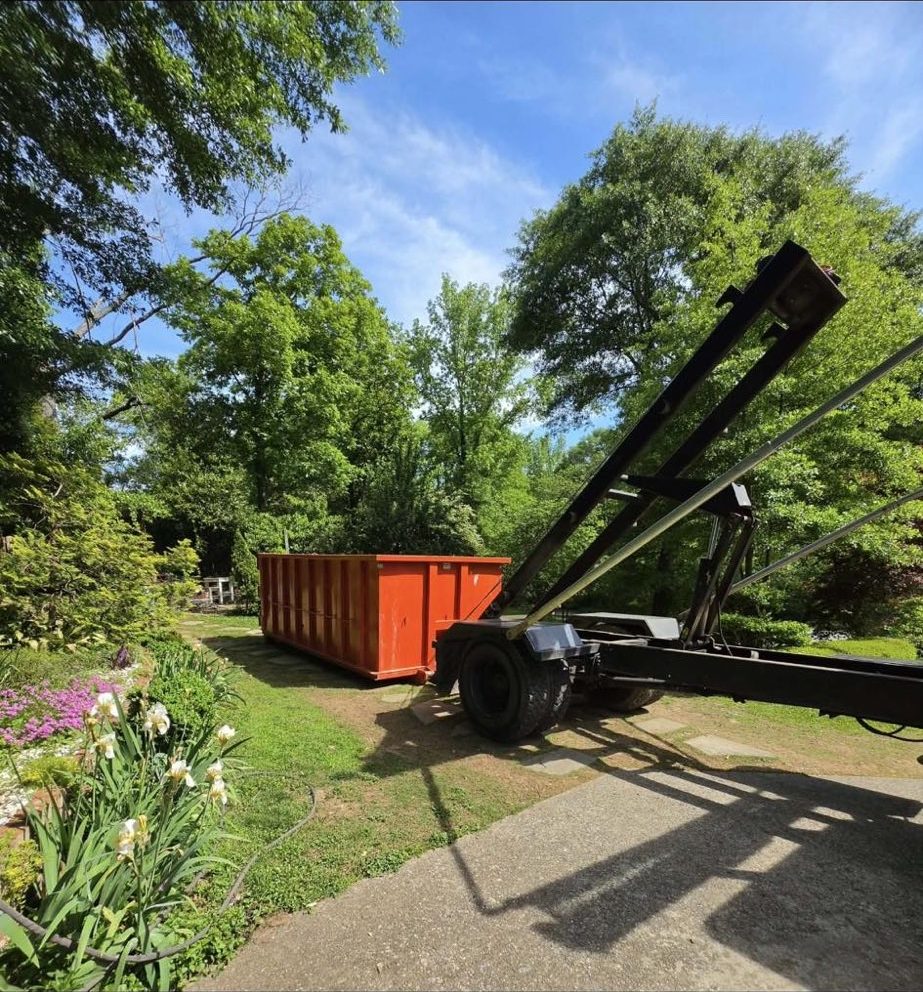 An orange Dutch Dumpsters roll-off container set on the grass beside a residential driveway in North Alabama.