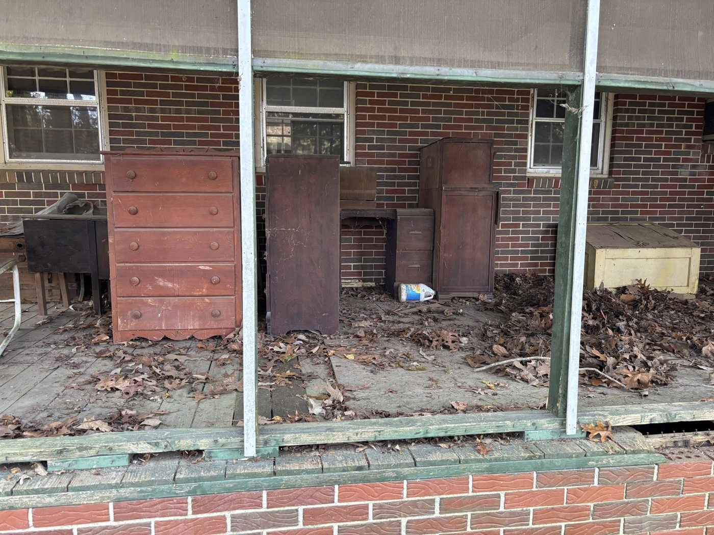 A covered porch stacked with old dressers, cabinets and leaf debris before a Dutch Dumpsters cleanout.