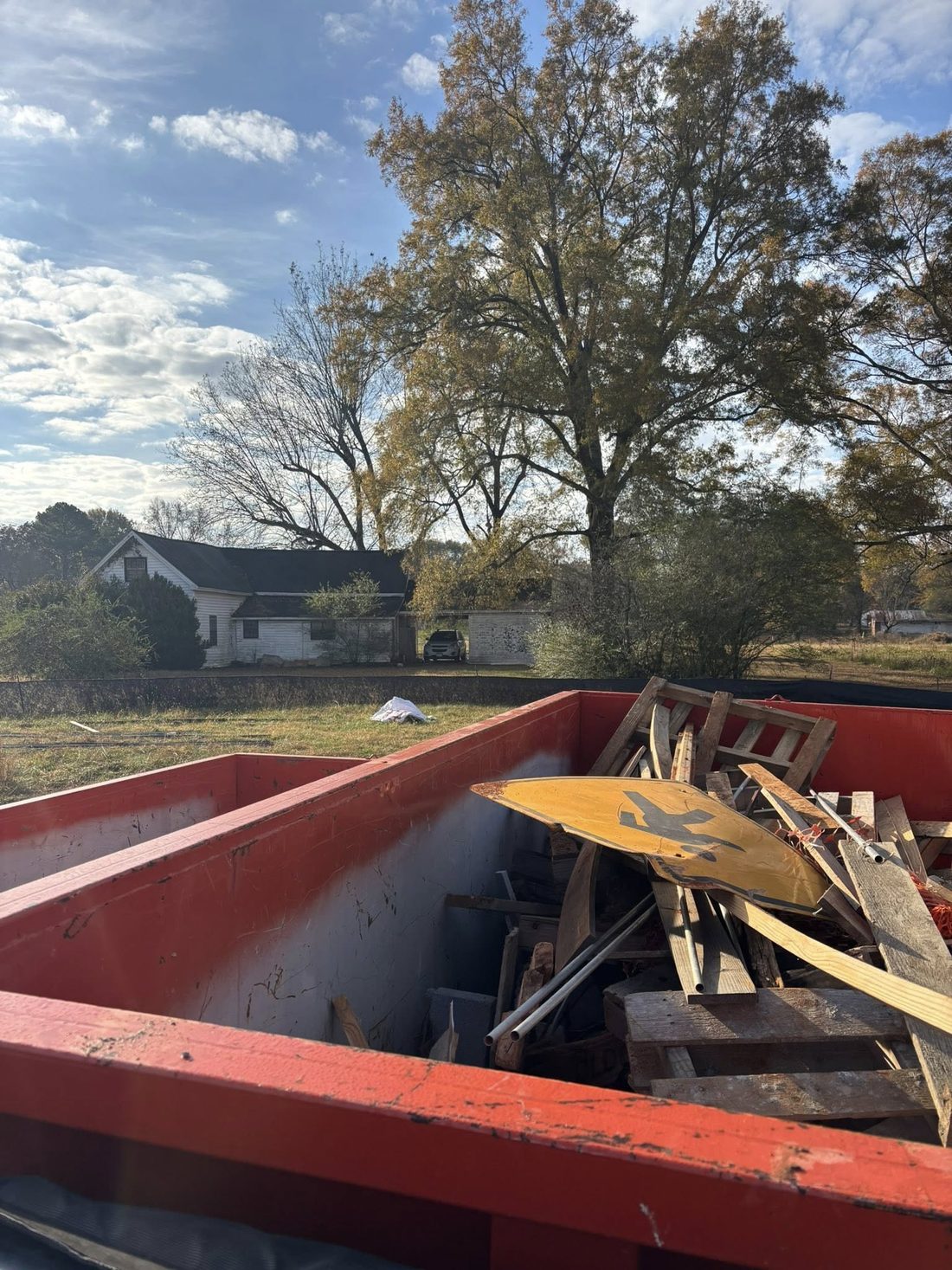 A Dutch Dumpsters roll-off container loaded with lumber and pallets on a rural Cullman County property.